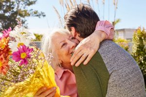 Older woman getting surprised with flowers by her son