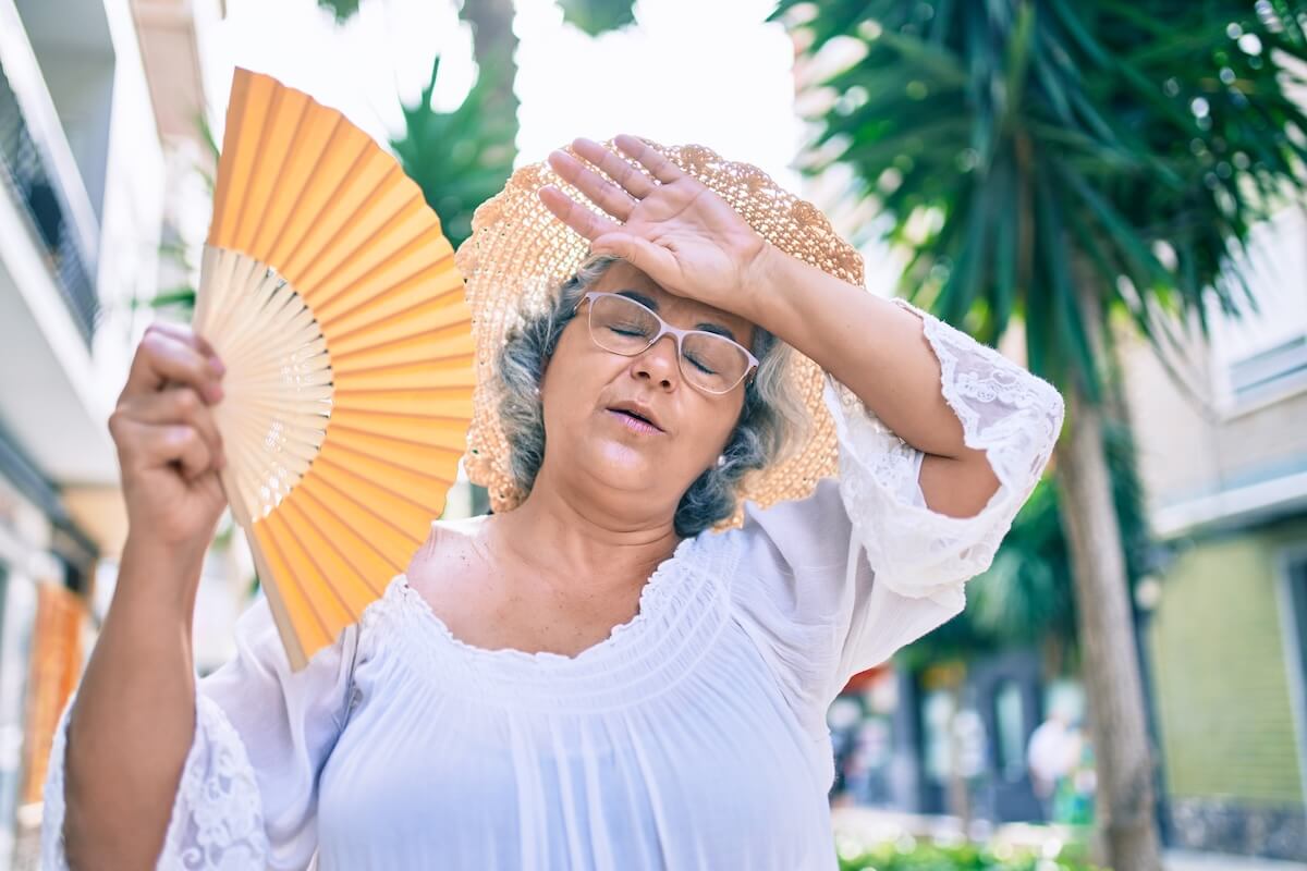 older woman fanning on the street | The Hampton at Meadows Place Older woman on the street with early signs of dehydration